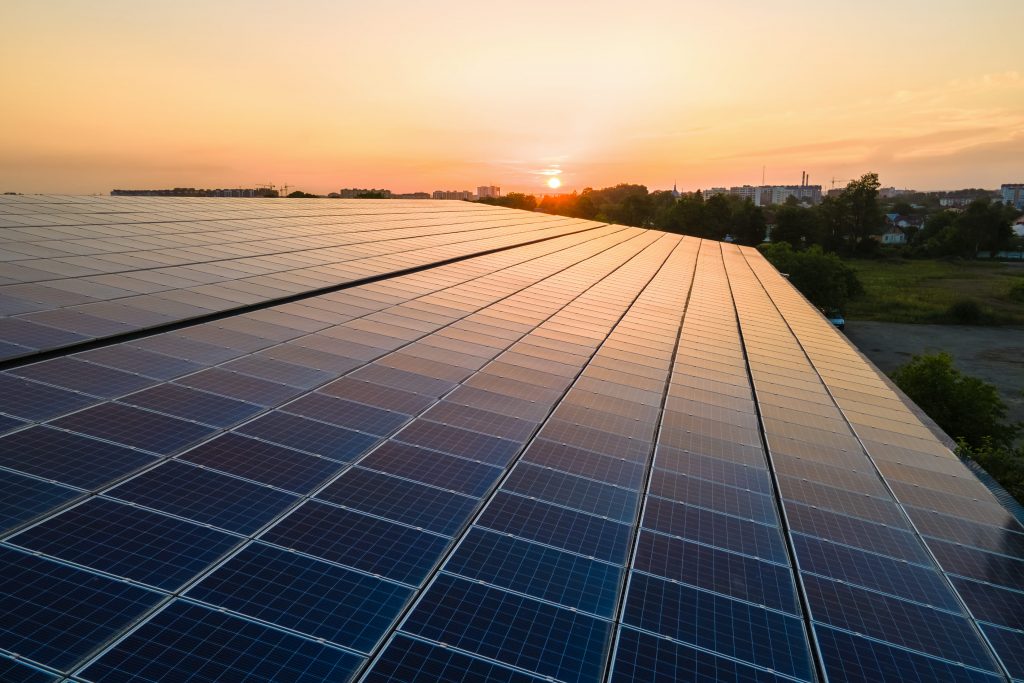 Painéis solares fotovoltaicos azuis montados no telhado do prédio para produzir eletricidade ecológica limpa ao pôr do sol. Conceito de produção de energia renovável.