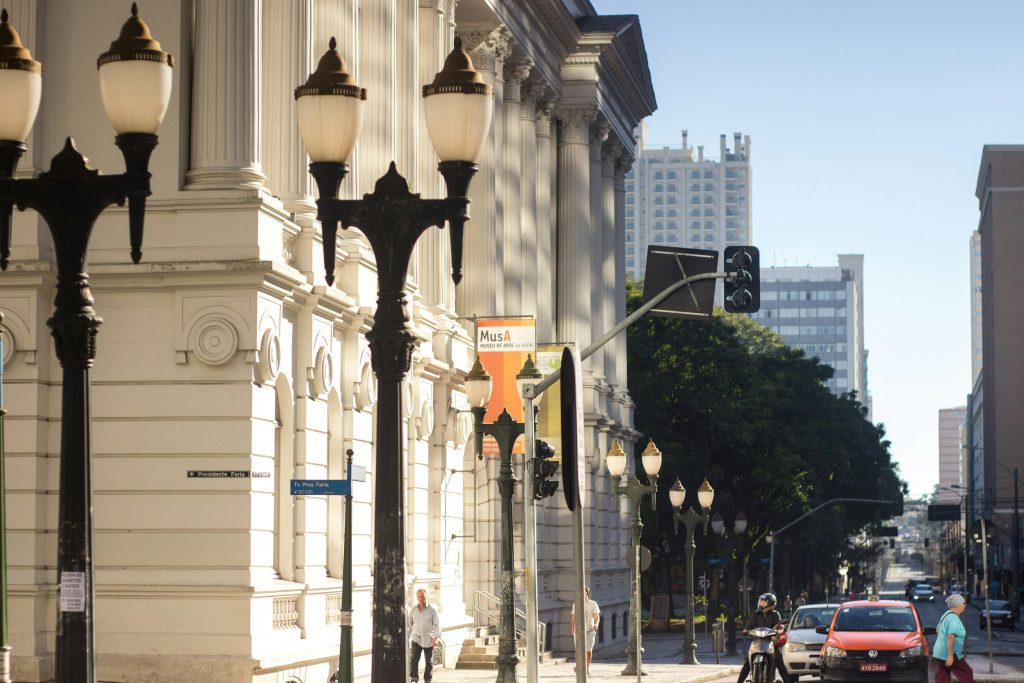 Imagem do prédio histórico da Universidade Federal do Paraná, com os tradicionais postes de luz e, ao fundo, prédios e carros. Veja dicas sobre a gastronomia em Curitiba!
